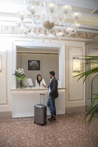 um homem com uma mala e uma mulher no balcão em Hotel Grande Italia em Chioggia