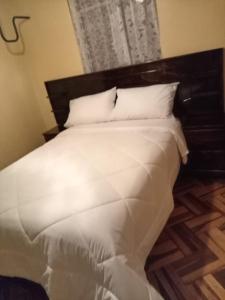 uma cama com lençóis brancos e almofadas num quarto em HOSTAL SUIT ANDINA em Puno