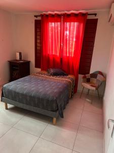 a bedroom with a bed with red curtains and a chair at Kama in Sainte-Luce