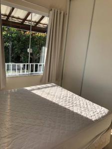 un letto bianco in una stanza con una finestra di CASA DE PRAIA NO CONDOMÍNIO PARAÍSO, GUARAJUBA a Camassari Altre 27 foto