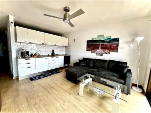 ein Wohnzimmer mit einem schwarzen Sofa und einer Küche in der Unterkunft Sasha Tenerife in Costa Del Silencio