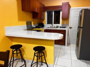 a kitchen with a white counter and two bar stools at Enjoy this Vacation Home close to the beach! in La Ceiba