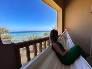 a woman sitting on a balcony looking out at the ocean at The Breakers Diving and Surfing Lodge Soma Bay in Hurghada
