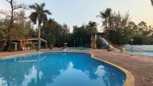 a large blue swimming pool with a slide and palm trees at Pinewood Resort in Karjat
