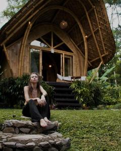 una mujer sentada en el césped delante de una casa en Arcada Bali Bamboo House en Sidemen