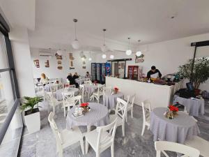 un restaurante con mesas blancas, sillas blancas y gente en Pensiune/Bistro ANNE MARIE, en Techirghiol