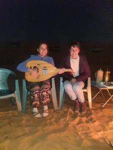três pessoas sentadas em cadeiras na areia com uma guitarra em Hamood desert local camp em Al Wāşil
