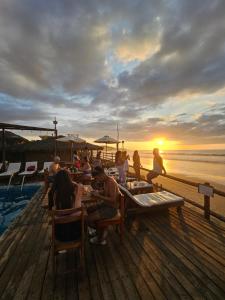 un grupo de personas sentadas en mesas en un muelle con la puesta de sol en The Point Mancora - Beach Party Hostel en Máncora