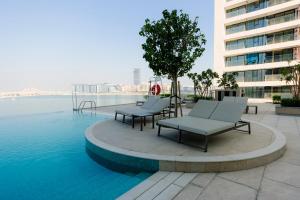 a pool with chairs and a tree on a building at Beachfront Elegant 2BD Condo with Breathtaking Views -15AB01 in Dubai