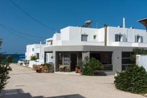 biały budynek ze stołami i krzesłami przed nim w obiekcie V-rooms in Milos Cyclades w mieście Pollonia