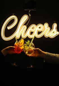 two hands holding two cocktails in front of a neon sign at Hotel Zacisze in Węgierska Górka