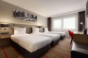 a hotel room with two beds and a desk at Ramada by Wyndham Amsterdam Airport Schiphol in Badhoevedorp