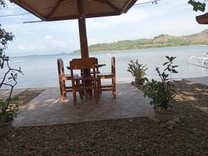 a table and chairs under an umbrella next to the water at Pelangi Homestay Bungalow Gili gede in Sekotong