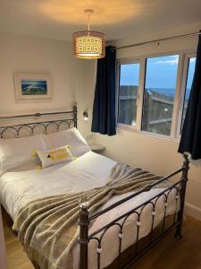 a bedroom with a bed with a chandelier and two windows at Citrus Chalet, modern light and airy! in Redruth