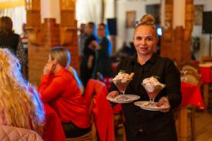 a woman holding two plates of ice creaminis at Pensiunea Koronka in Corunca