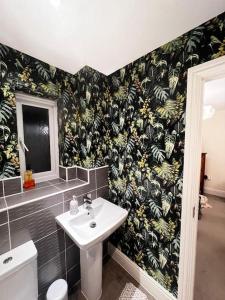 a bathroom with a sink and a wall with a tropical wallpaper at Fairford House - 4 Bed House - Close to the Racecourse in Cheltenham