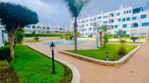 un complexe avec une piscine, des palmiers et un bâtiment dans l'établissement Kabila Vista par IMMO MARINA Vacances de rêve R, à M'diq