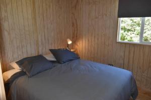 a bedroom with a bed with blue pillows and a window at Beautiful Don Pedro Cabin, Chilean Patagonia. in Chaitén