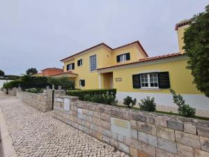 une maison jaune avec un mur en pierre à côté d'une rue dans l'établissement Casa Da Luz Villa - Praia D'El Rey Golf Resort, à Casal da Lagoa Seca