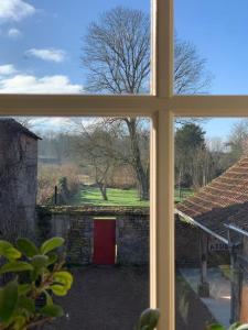 een raam met uitzicht op een tuin met een rode deur bij La maison du Boulanger in Pontaubert