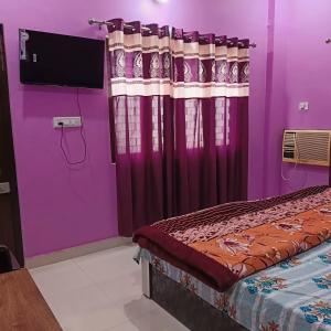 um quarto com paredes roxas e uma cama com uma televisão em Saraswati Sadan Homestay Ayodhya em Faizābād