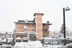 ピンツォーロにあるHotel Cristinaの雪に停められた車を置いた大きなレンガ造りの建物