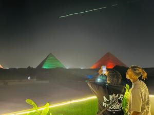 duas pessoas tirando uma foto das pirâmides à noite em Capital Of Pyramids Hotel no Cairo