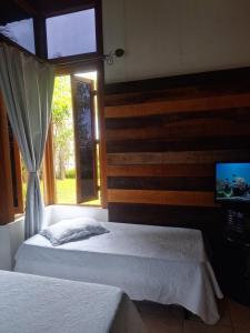 a bedroom with two beds and a window and a television at Pousada ESQUINA DO ATLANTICO SUL in Tubarão