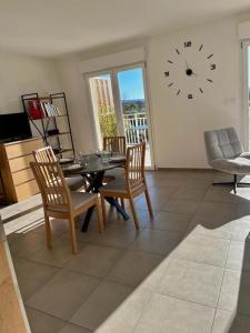 ein Esszimmer mit einem Tisch, Stühlen und einer Uhr in der Unterkunft Appartement avec Terrasse in Cléon-dʼAndran