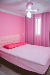 een roze slaapkamer met een bed en een plafondventilator bij Apartamento rosa in Guarapari