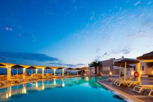 a pool with lounge chairs and umbrellas at night at Kavuras Village Hotel & Suites in Agios Prokopios
