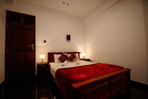 a bedroom with a bed with red sheets and two lamps at Adams Peak Inn in Nallathanniya