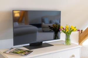 telewizor z płaskim ekranem siedzący na stole z kwiatami w obiekcie Plas Robin w mieście Llandyssil
