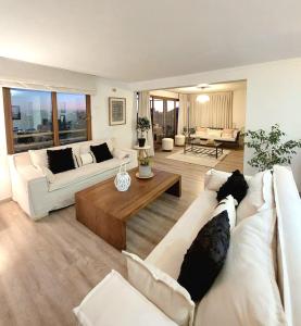 una sala de estar con 2 sofás blancos y una mesa. en Hermoso y amplio departamento en las Condes Parque Arauco, en Santiago