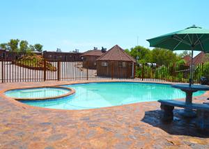 een zwembad met een parasol en een bank bij Crocodile Pools Resort in Gaborone