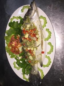 um prato de comida com um peixe com molho e legumes em จอมเมือง Motel em Nan