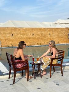 twee vrouwen in badpakken aan een tafel bij een zwembad bij Desert Camps Heritage Jaisalmer in Jaisalmer