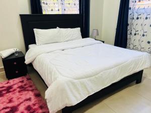 a bedroom with a large bed with white sheets and a pink rug at Oaklands Apartments in Morogoro