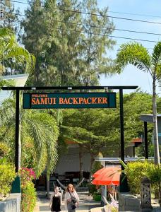 two women walking under a sign that reads sammut back packer at Samui Backpacker Hotel in Bangrak Beach