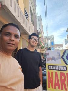 Dois homens estão em frente a um sinal. em Narmada Guest House em Indore