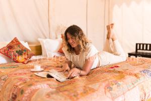 a woman laying on a bed reading a book at Desert Dream Royal Camp with Pool in Jaisalmer