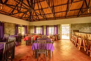 a dining room with tables and chairs and windows at Mise cave lodge in Kapchorwa