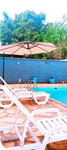 un par de sillones y una sombrilla junto a una piscina en HOTEL JP, en Delfinópolis