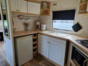 a small kitchen with white cabinets and a window at Stacaravan 14 met airco vakantiepark de Tien Heugten Schoonloo Drenthe in Schoonloo