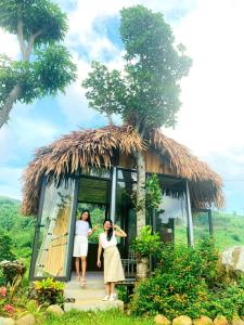 duas mulheres à porta de uma pequena cabana com uma árvore em Ngòi Xanh Ecolodge (Bungalow - Restaurant - Coffee) em Tuyên Quang