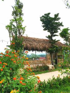 a building with a straw roof with flowers in front of it at Ngòi Xanh Ecolodge (Bungalow - Restaurant - Coffee) in Tuyên Quang