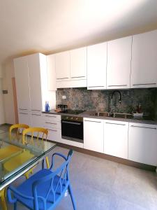 una cocina con armarios blancos y una mesa y sillas de cristal. en Casa del Cigno, en Monterotondo