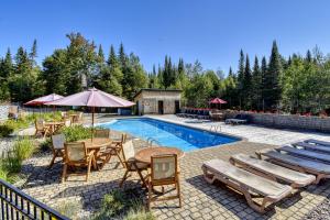 una piscina con sillas, una mesa y una sombrilla en Luxurious log cabin with private spa, en Lac-Supérieur
