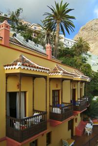 a yellow house with balconies and a palm tree at Hotel Jardín Concha in Valle Gran Rey