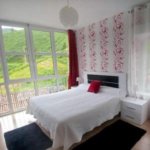 um quarto com uma cama branca e uma almofada vermelha em Alojamiento rural El Refugio em Tudanca